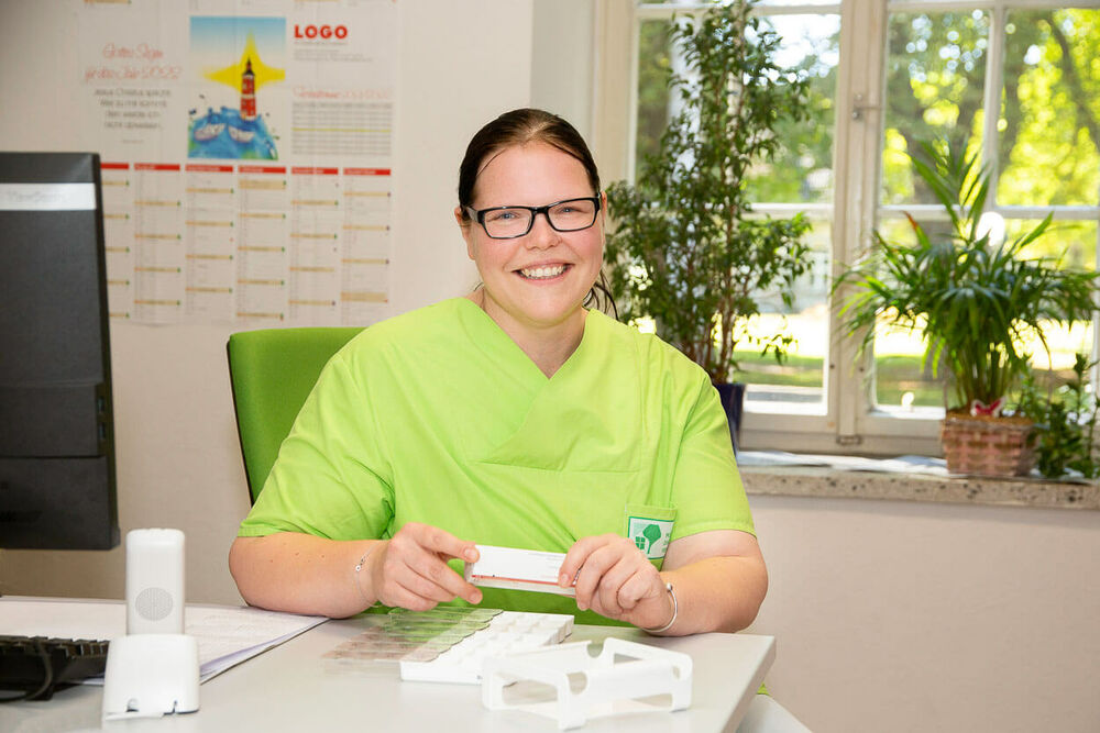 Eine Mitarbeiterin unseres Pflegedienst Greifswald sortiert Medikamente und lächelt in die Kamera.