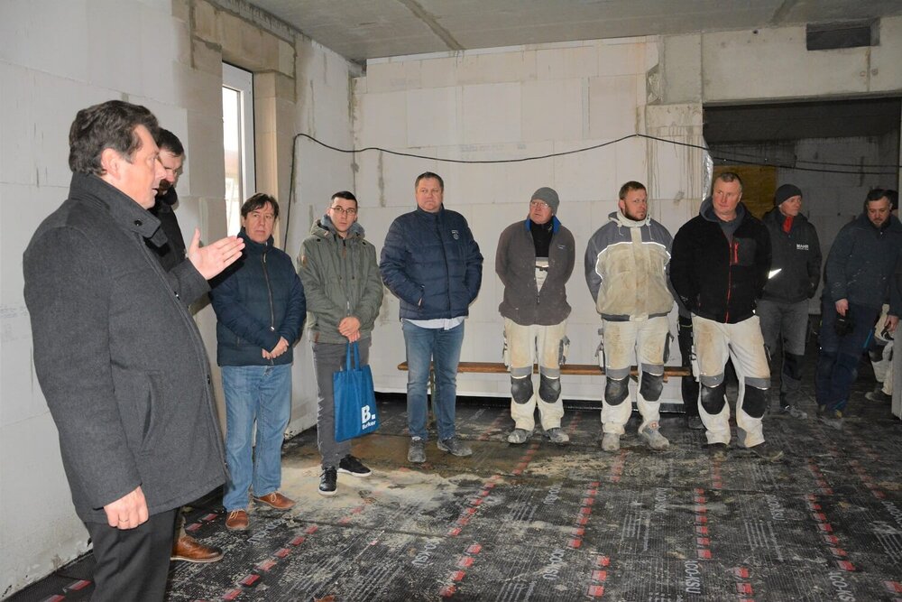 Eine Gruppe von Menschen in Handwerkskleidung steht in einem Raum im Rohbau