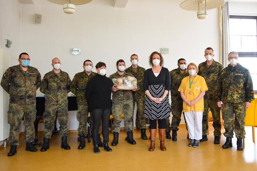 Eine Gruppe Soldaten in Uniform steht zusammen mit drei Frauen in Dienstkleidung in einem großen Raum