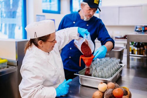 Eine Köchin und ein Helfer füllen frischen Fruchtaufstrich in Gläser ab