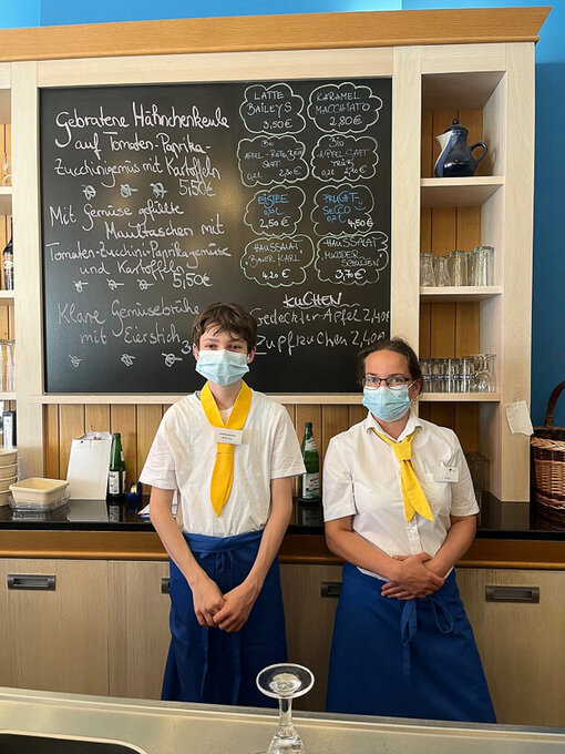 Eine Frau und ein Junge in Servicekleidung stehen vor dem Tagesaushang des Café und Restaurant Lichtblick