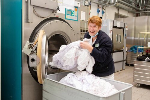Eine Mitarbeiterin lächelt und holt eine große Wäschemenge aus einer Waschmaschine