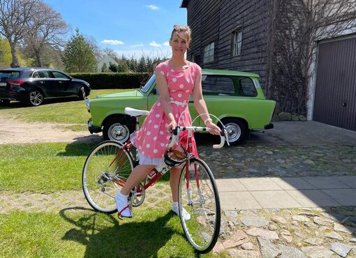 Eine Frau in einem sommerlichen Kleid steht vor ihrem Fahrrad