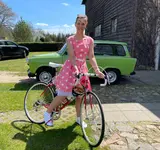 Eine Frau in einem sommerlichen Kleid steht vor ihrem Fahrrad