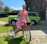 Eine Frau in einem sommerlichen Kleid steht vor ihrem Fahrrad