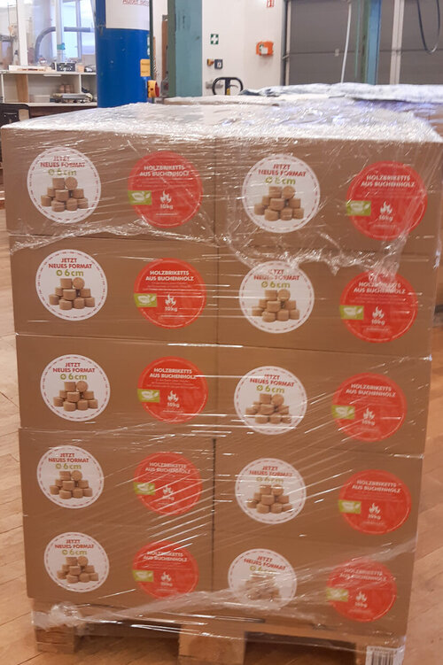 Mehrere Kartons mit Holzbriketts stehen gestapelt auf einer Palette zur Auslieferung