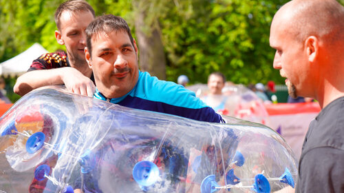 Ein Mann wird von zwei Helfern bei einem Lauf in einem großen Luftball unterstützt