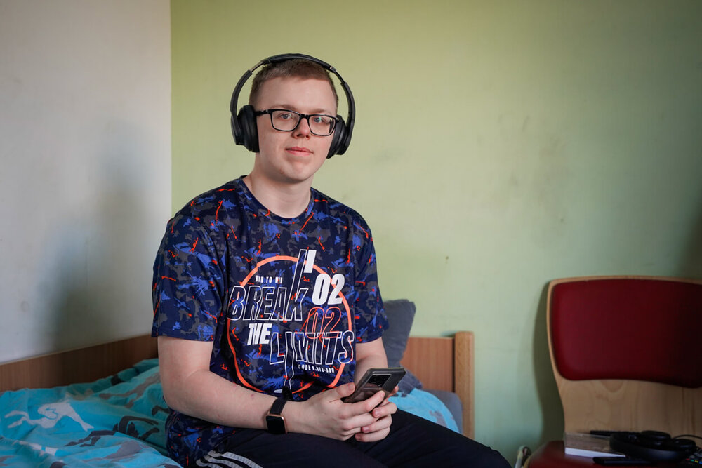 Ein junger Mann sitzt mit Kopfhörern auf seinem Bett und hat ein Smartphone in der Hand