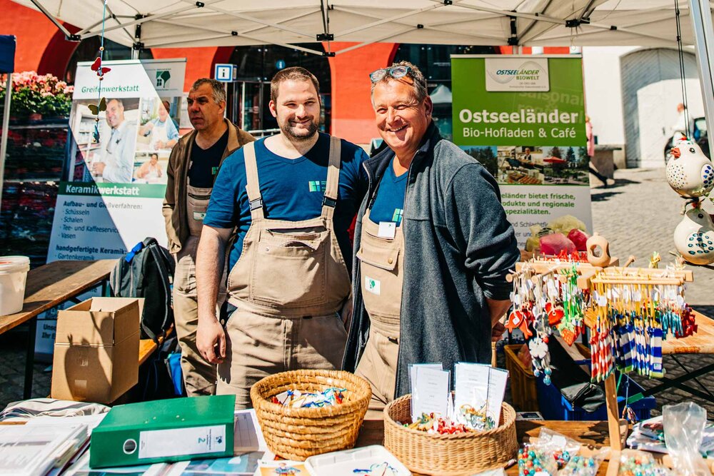 Zwei Männer mit T-Shirts des Pommerschen Diakonievereins stehen unter einem Pavillon