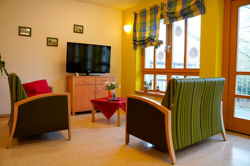 Ein Raum mit Sesseln, Tisch, Fernsehen und Bildern an der Wand vermittelt eine gemütliche Wohnatmosphäre