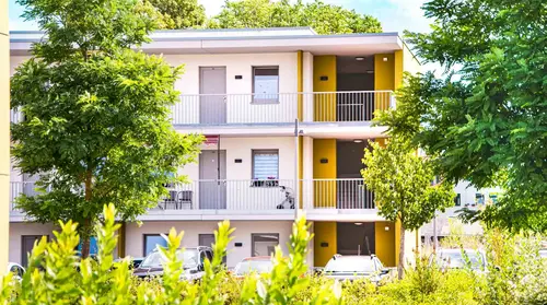 Blick auf einen Flügel eines Wohngebäudes des Senioren- und Wohnzentrums hinter zwei großen Bäumen und Büschen.