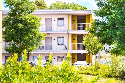 Blick auf einen Flügel eines Wohngebäudes des Senioren- und Wohnzentrums hinter zwei großen Bäumen und Büschen.