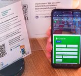 Ein Smartphone mit dem Check-In Formular des Hygiene-Rangers und ein erklärender Aufsteller