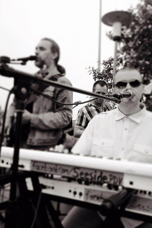 Renaldo Wandt sitzt am Keyboard und singt in ein Mikrofon. Micha Turban spielt im Hintergrund Gitarre und singt ebenfalls.
