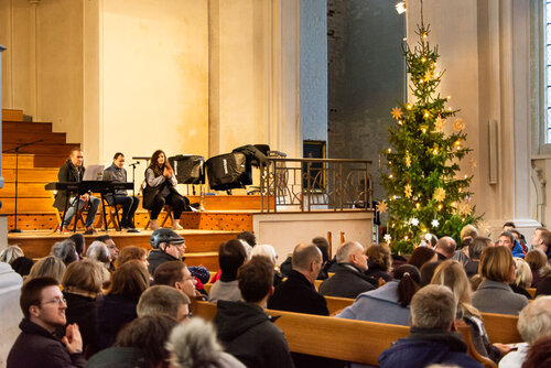 Menschen in Kirchenbänken vor einem Tannenbaum. Auf der Bühne die Musikerinnen und Musiker von Seeside