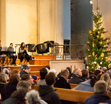 Menschen in Kirchenbänken vor einem Tannenbaum. Auf der Bühne die Musikerinnen und Musiker von Seeside