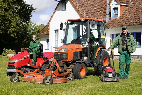 Zwei Männer mit Rasenmäher, Sitzrasenmäher und Traktor auf einem Rasen
