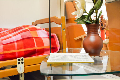 Ein Bett steht vor einem Glastisch, auf dem ein Prospekt liegt und eine Blume in einer Vase steht.