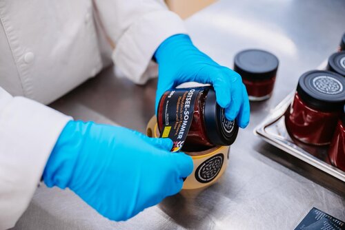 Eine Mitarbeiterin klebt ein Etikett auf ein Einmachglas mit Fruchtaufstrich