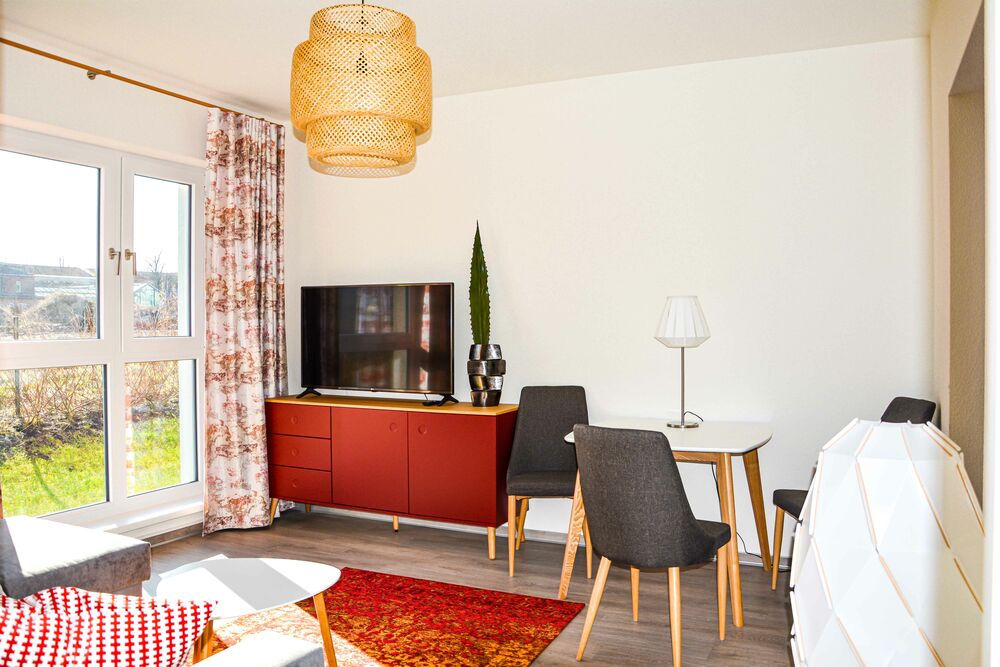 Wohnzimmer mit Teppich, Tisch, Stühlen, TV, Schrank und Lampe