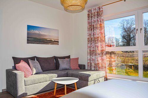 Wohnzimmer mit Couch, Tisch, Wandbild, Stühlen, Gardinen und Aussicht