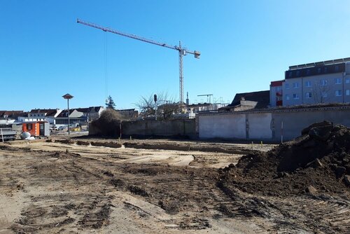 Ein große Fläche Erde mit einem aufgeschütteten Erdhügel und im Hintergrund ein Kran