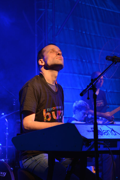 Marko Simanowski sitzt bei einem Konzert am Keyboard und reckt den Hals nach oben