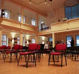 Ein großer Saal wie in einem Theater, in dem viele einzelne Stühle stehen