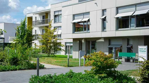 Außenansicht der Gebäudeanlage mit einigen Bäumen und Büschen und einem kleinen Fußweg