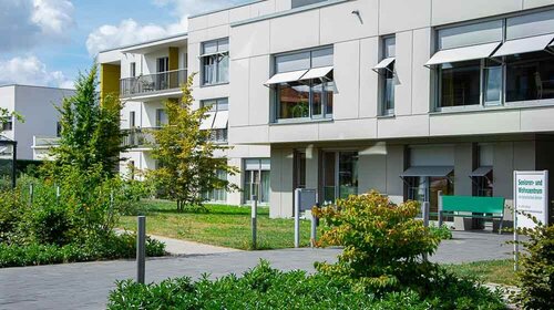 Außenansicht des Senioren- und Wohnzentrums am Botanischen Garten Außenansicht der Gebäudeanlage mit einigen Bäumen und Büschen und einem kleinen Fußweg