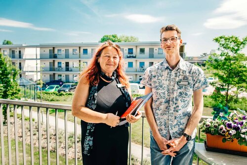 Eine Mitarbeiterin und ein Mitarbeiter stehen vor dem Gebäude und schauen den Betrachter an
