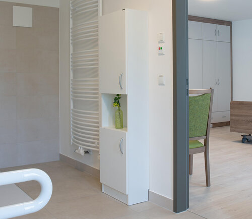 Ein Badezimmer mit ebenerdiger Dusche, Behindertengerechter Toilette, Handtuchtrockner und Schrank